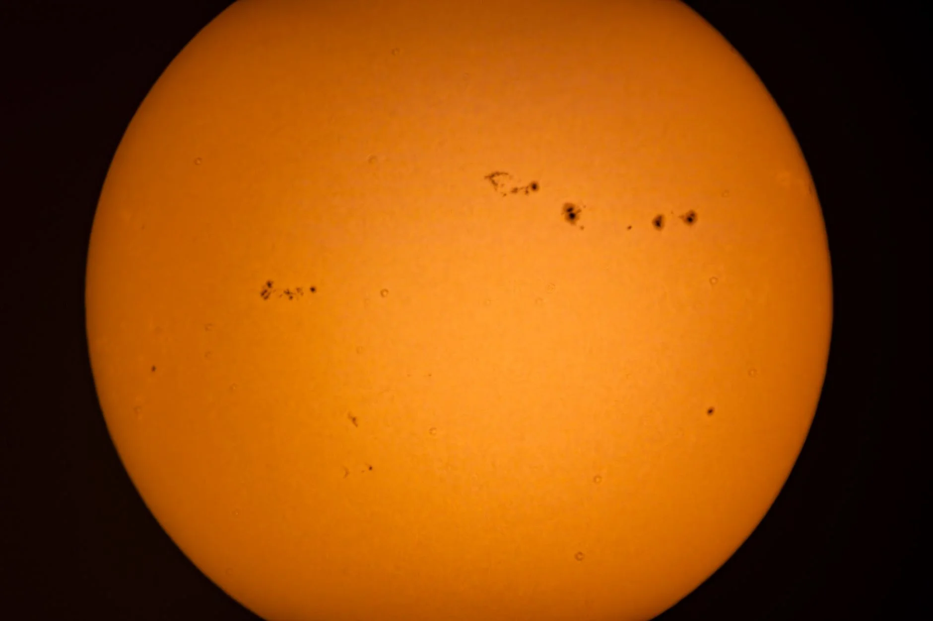 Photograph of the Sun through a solar filter showing several groups of dark sunspots