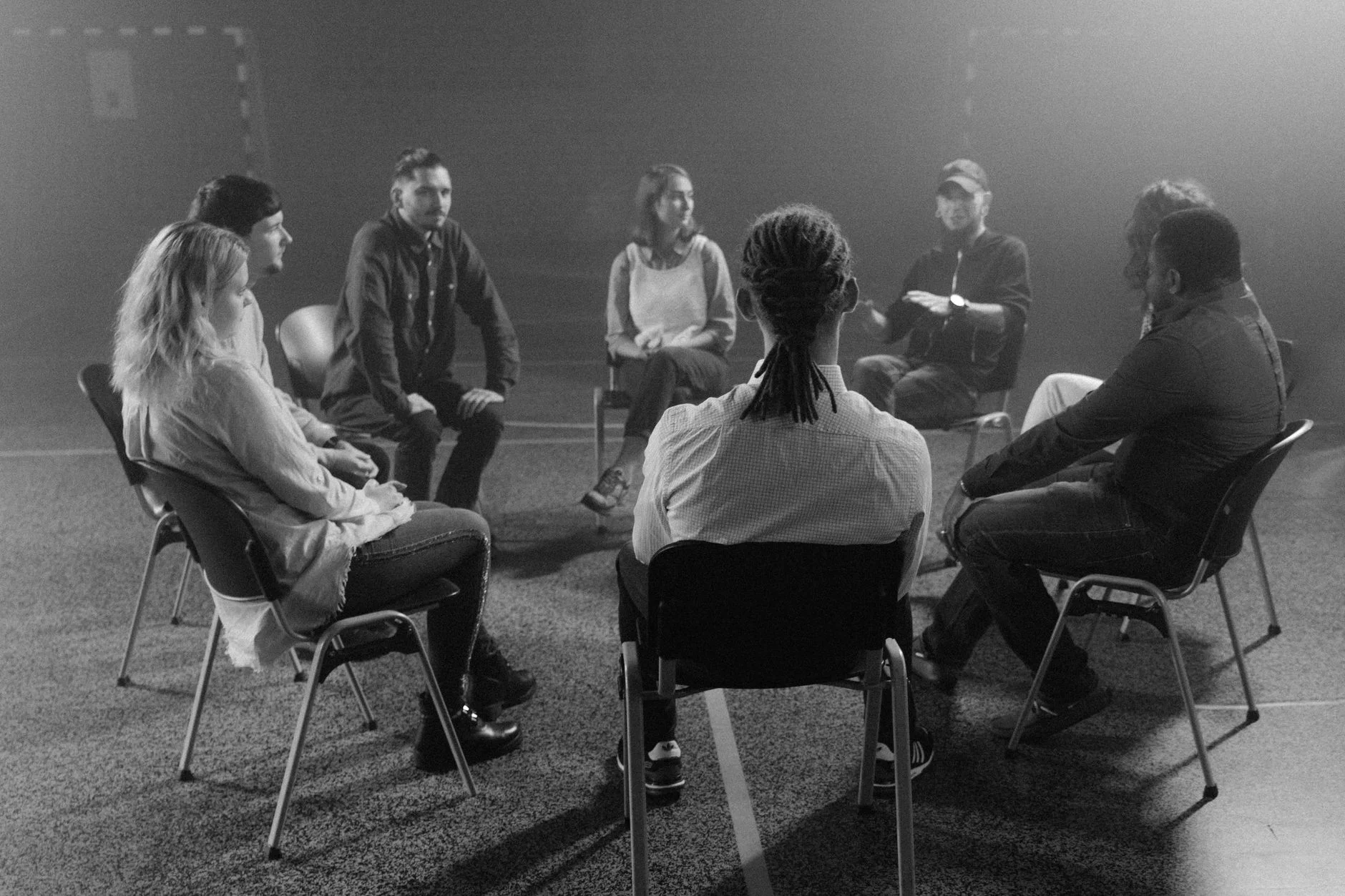 A group of adults sitting in a circle of chairs talking together