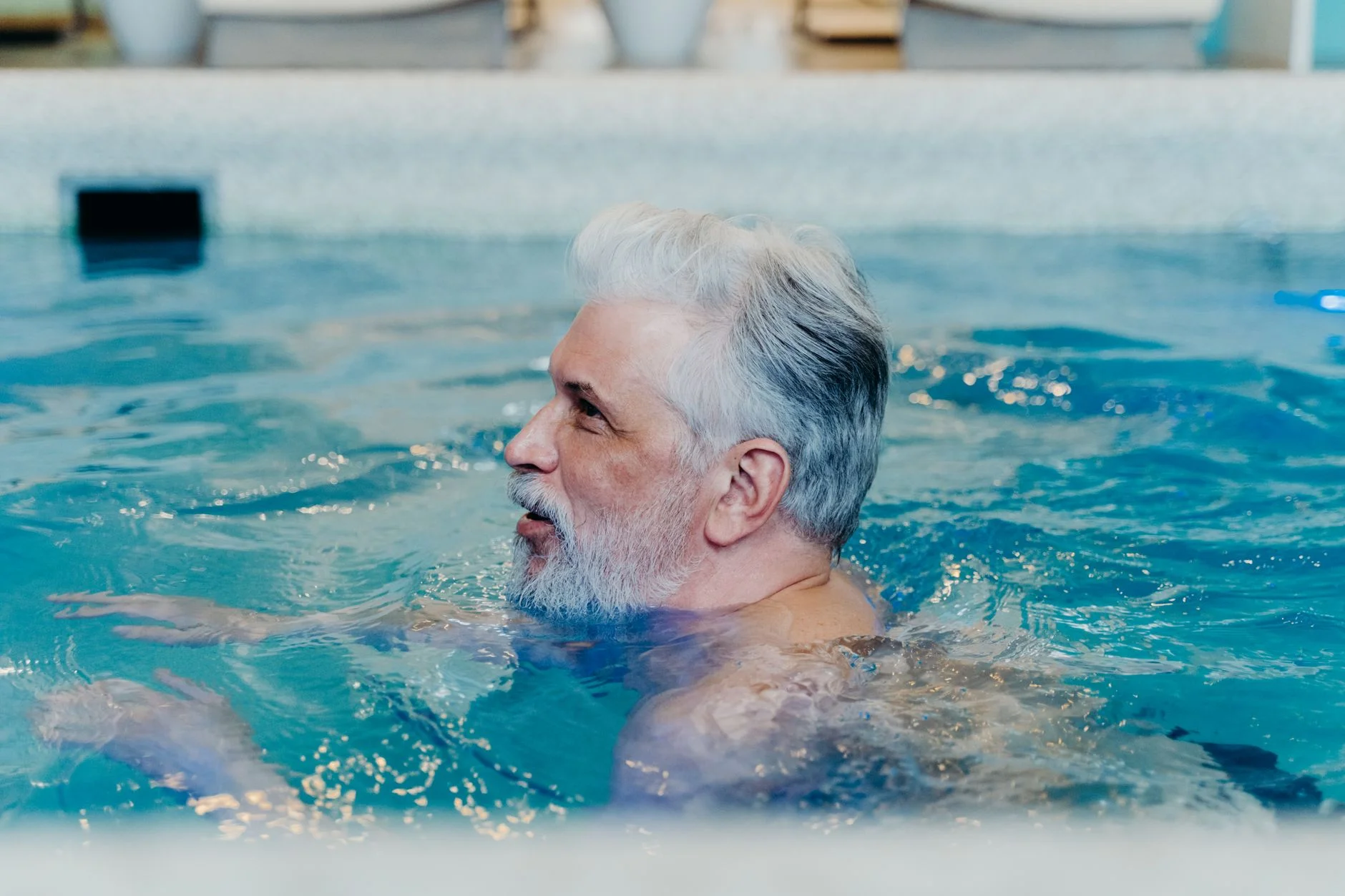 A grey-haired man swimming in a clear blue indoor pool