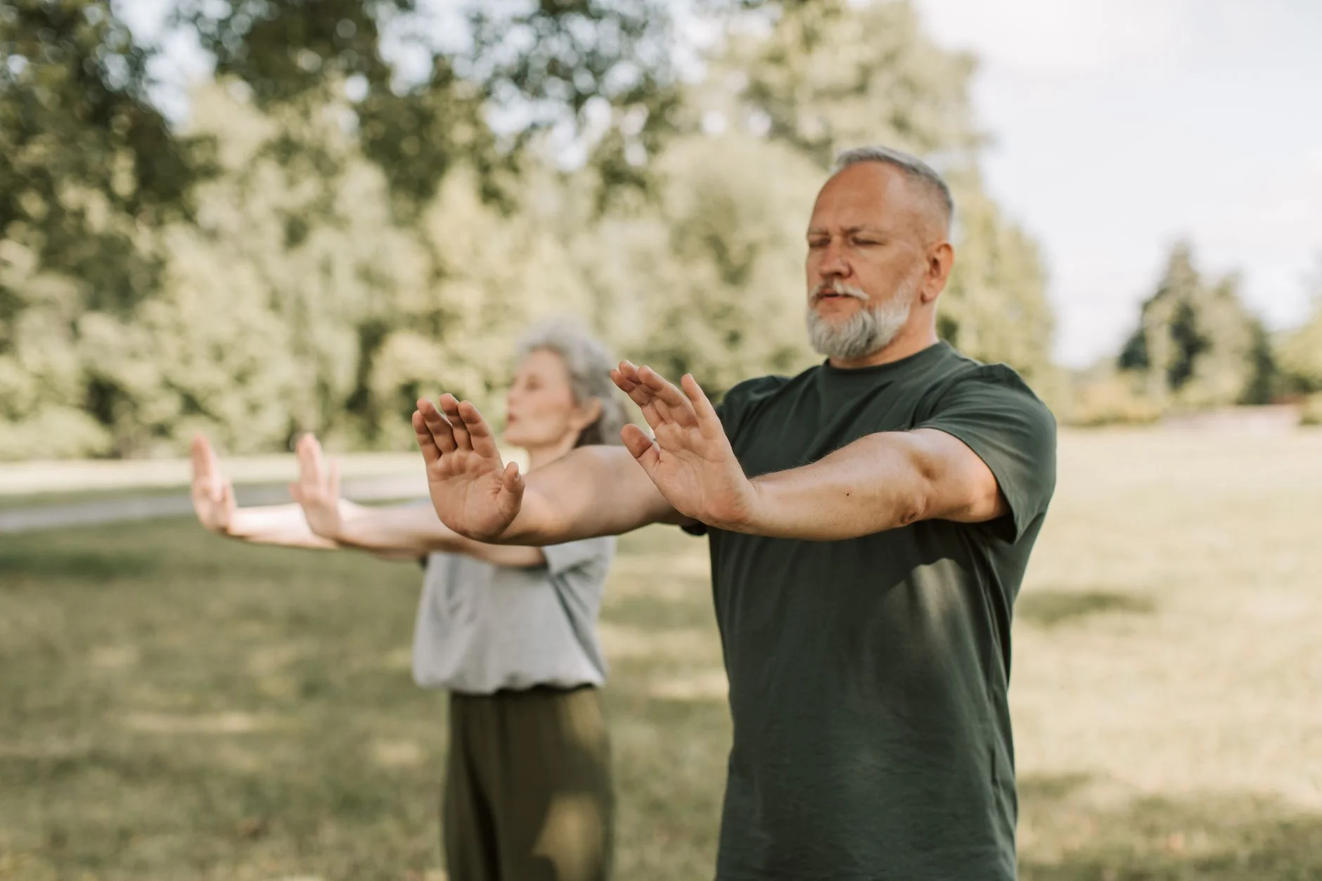 Two older adults practising slow, controlled tai chi-style arm movements on a lawn