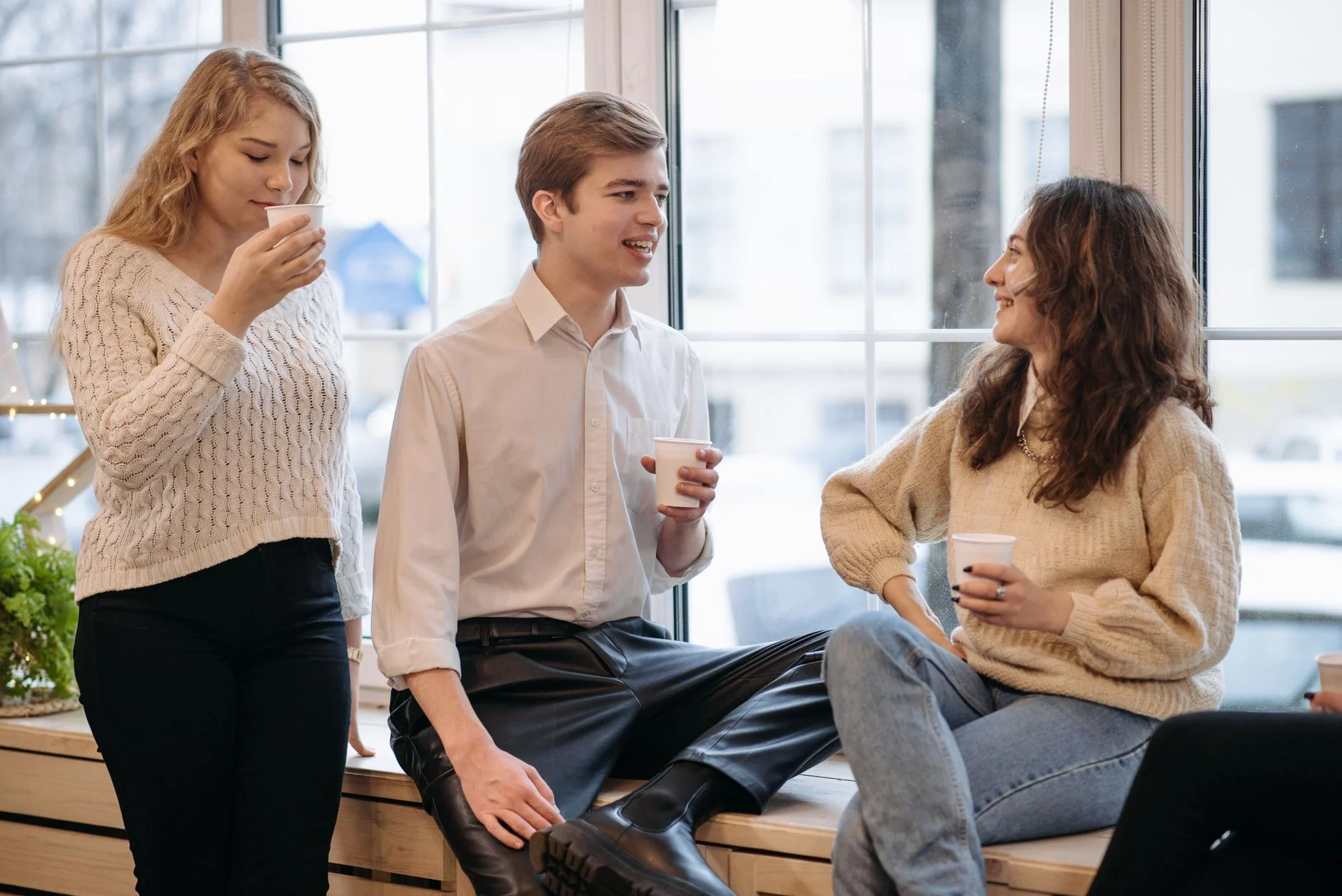 Three young adults chatting and drinking coffee by a window