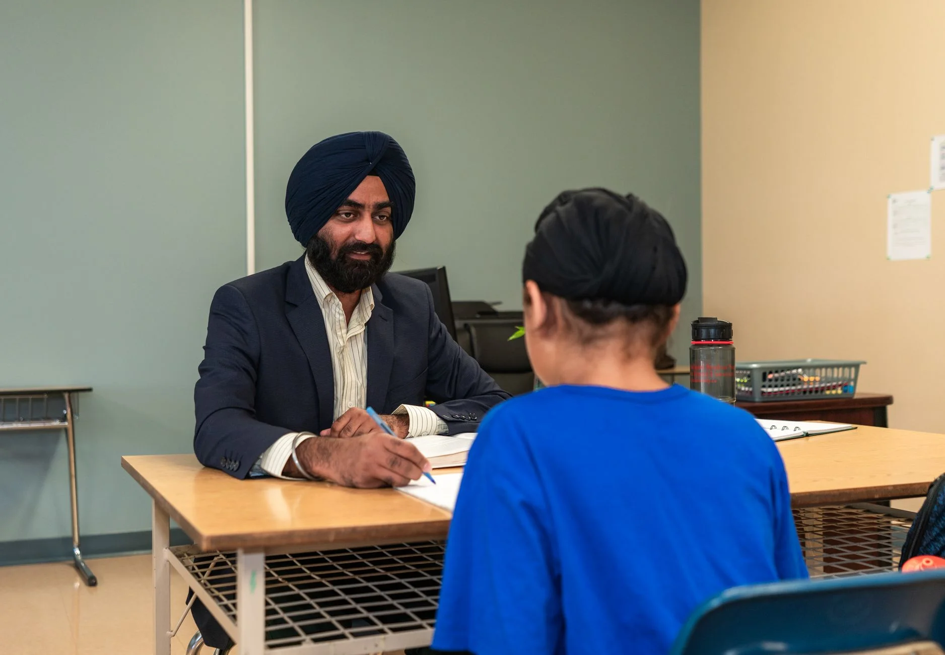 A teacher sitting at a desk and talking one to one with a student in a classroom