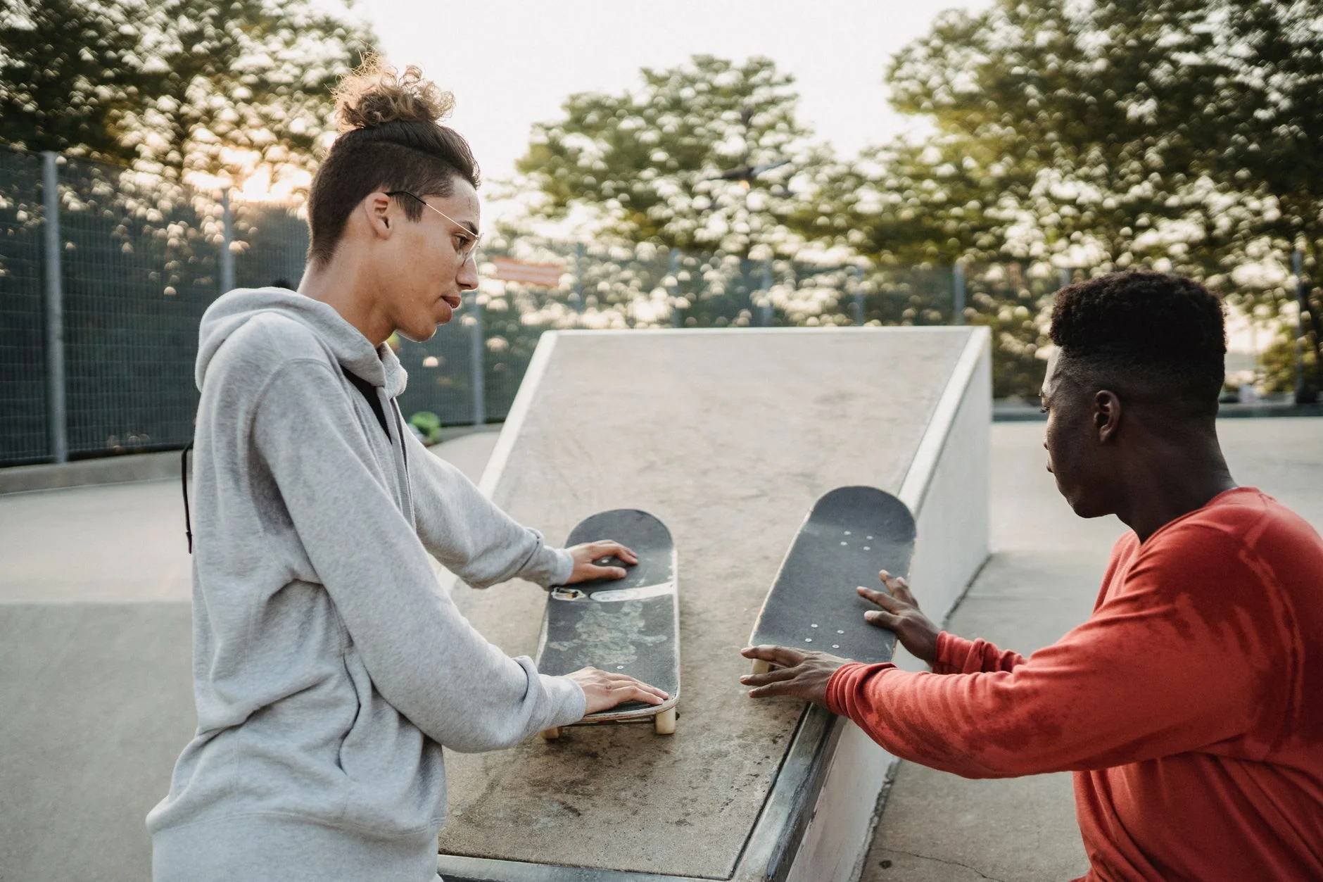 Two teenagers at a skate park leaning on their skateboards and chatting