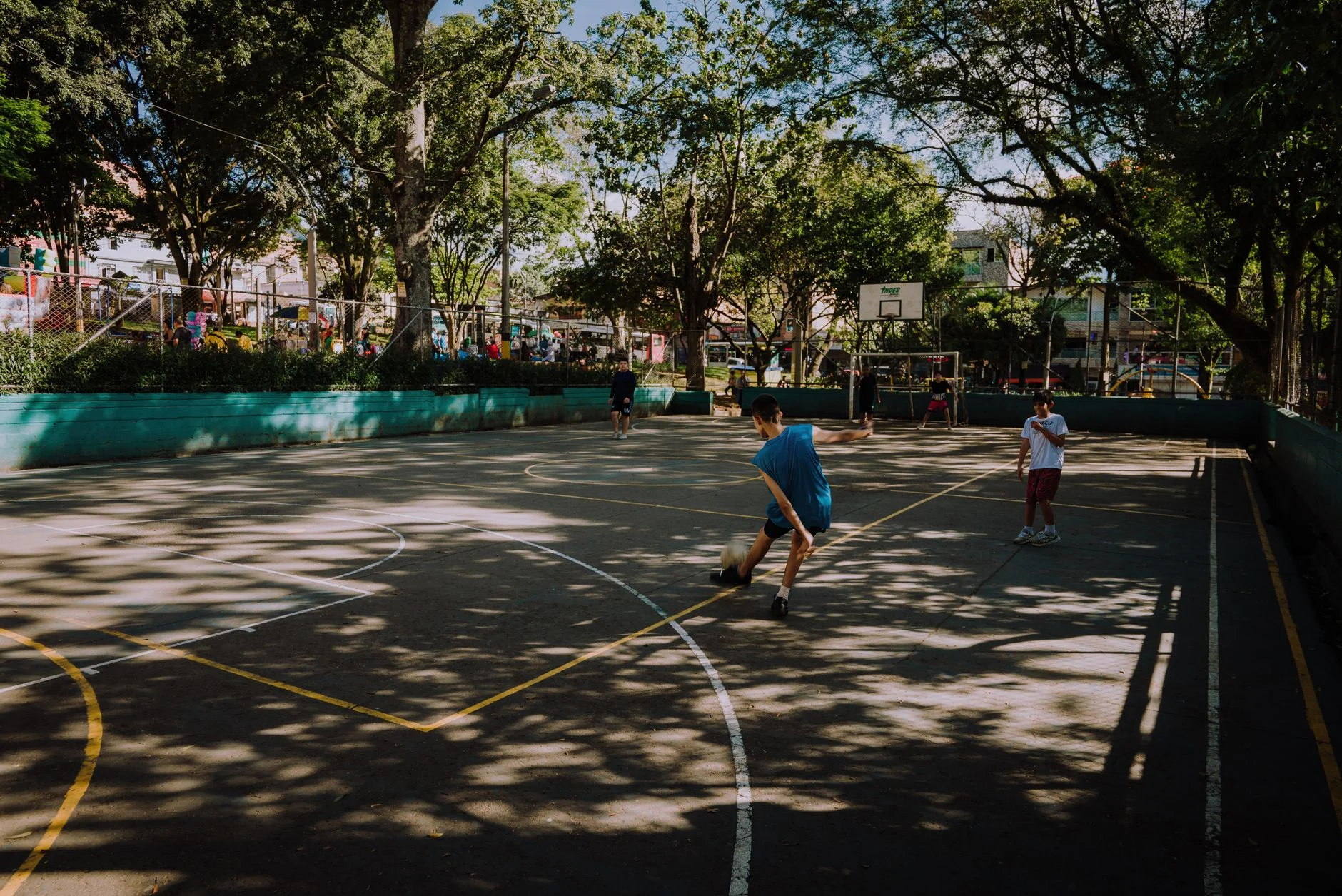 Teenagers playing football on a park court shaded by trees
