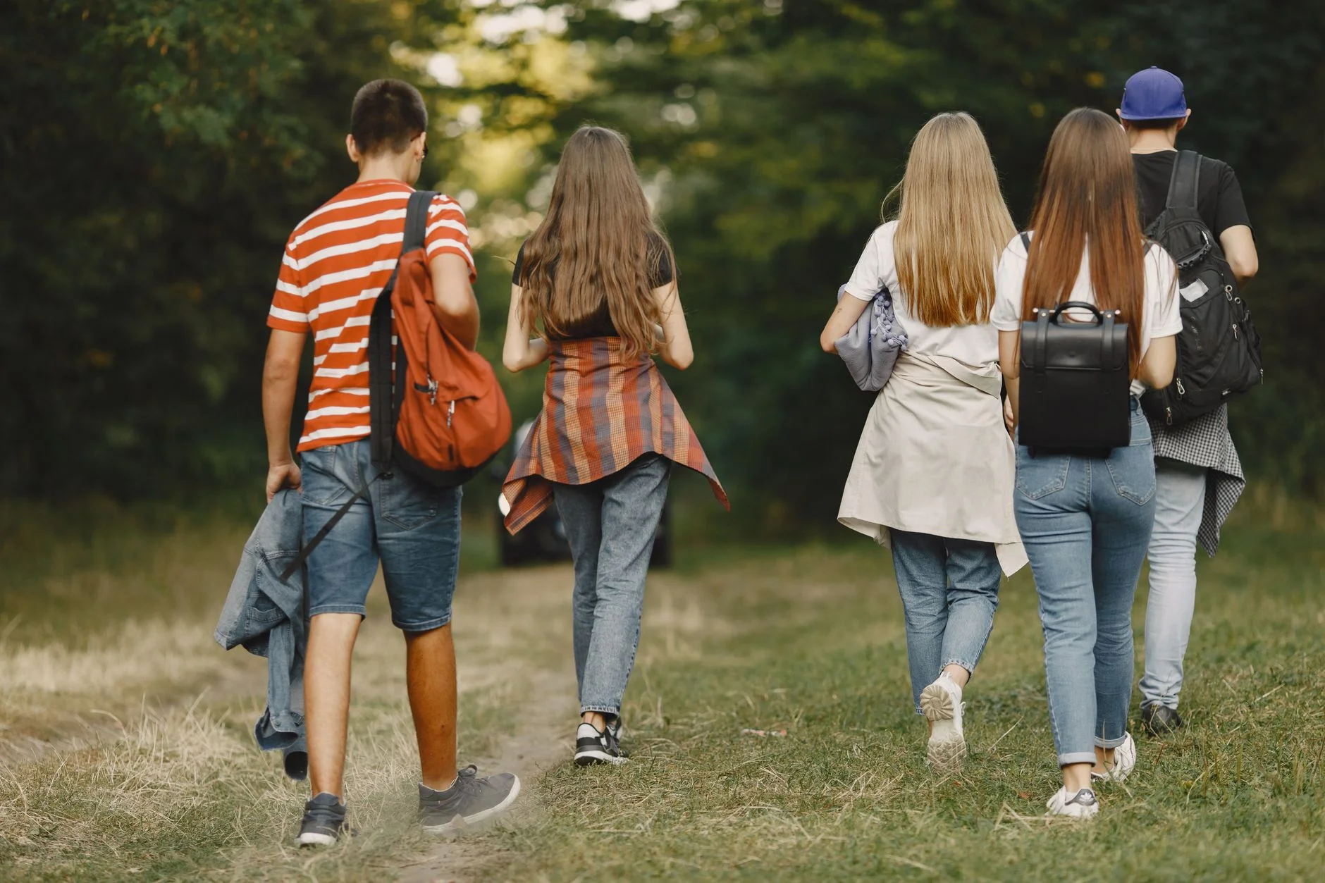 Four teenagers with backpacks walking together along a grassy path in a park