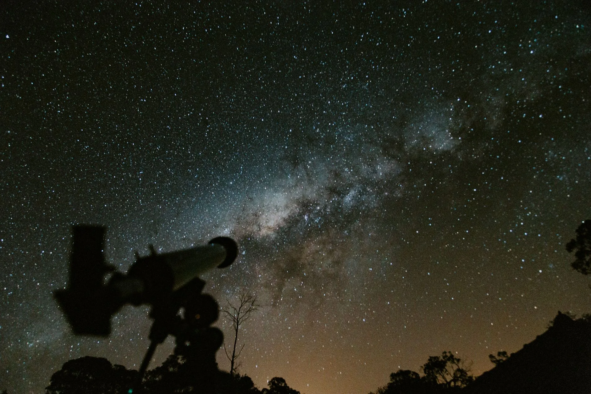 A telescope silhouetted against a night sky full of stars and the band of the Milky Way