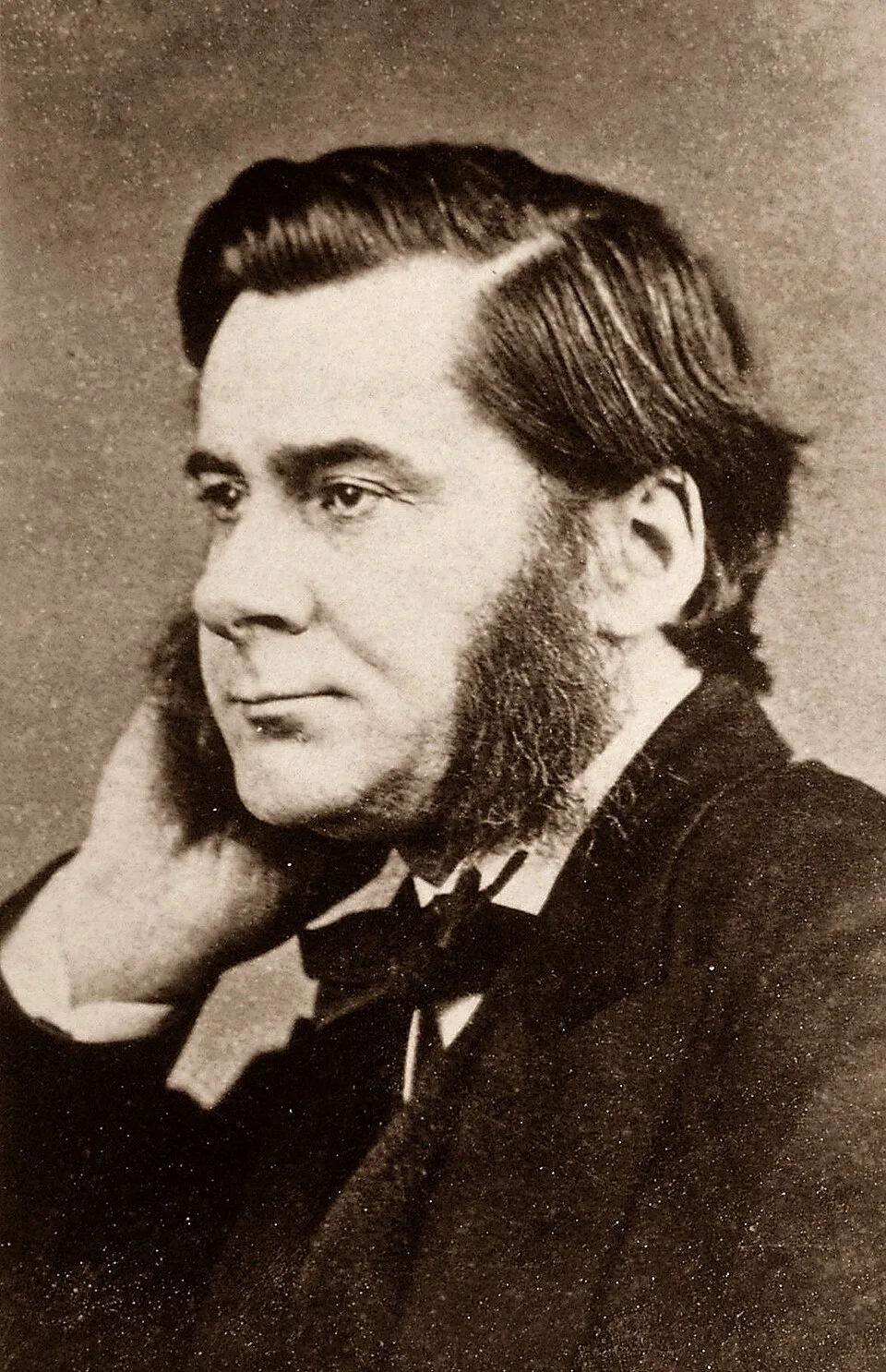 Black and white photograph of Thomas Henry Huxley with dark hair and side whiskers, resting his head on his hand, 1874