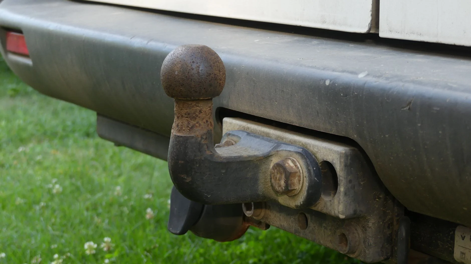 Close-up of a rusty swan-neck tow ball bolted under a car’s rear bumper