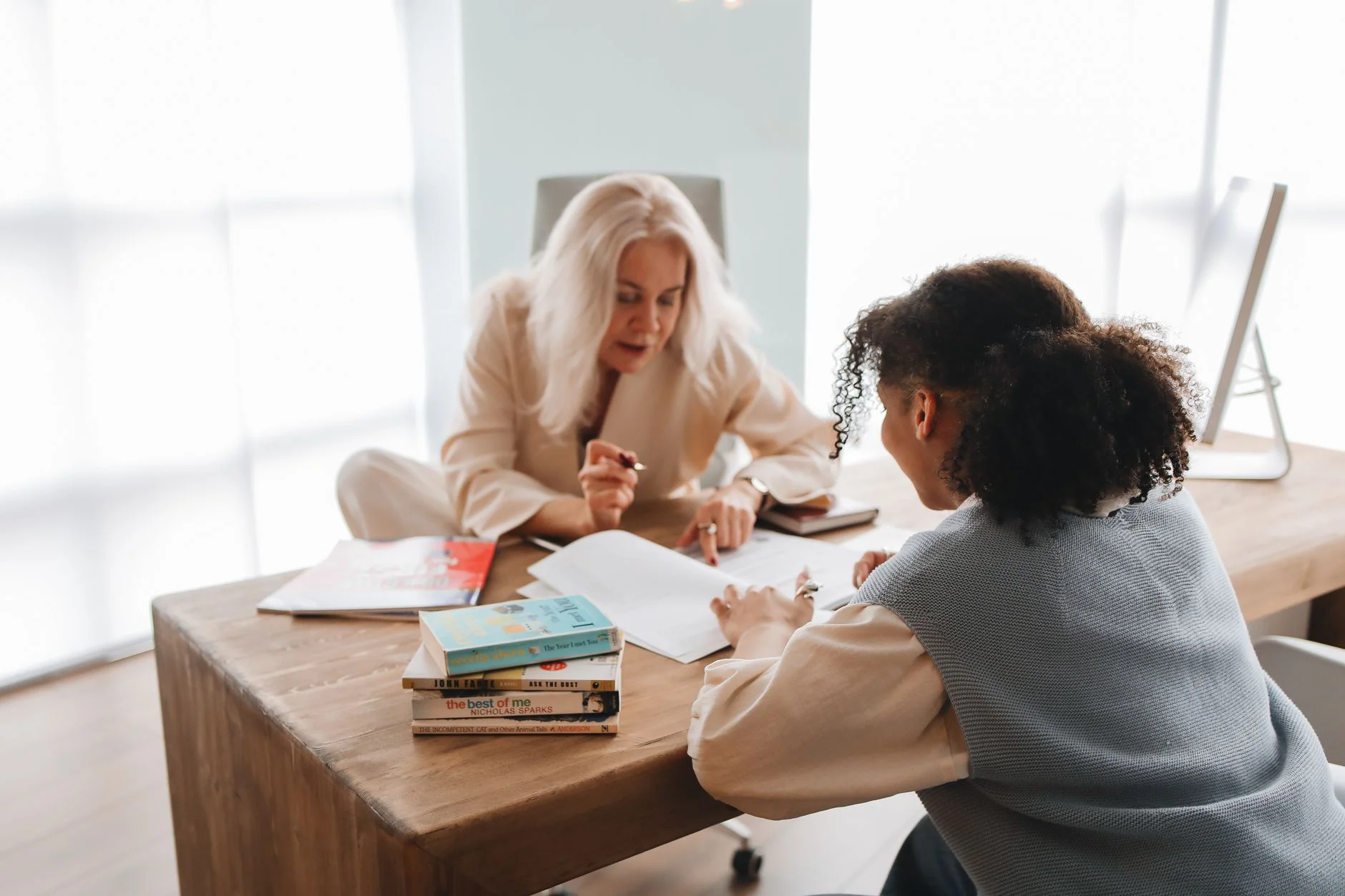A tutor and a student working together over papers and books at a wooden desk