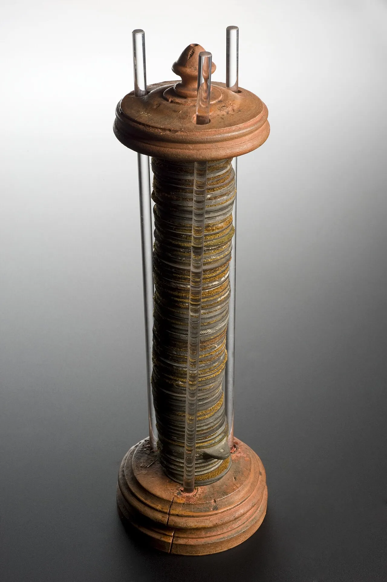 A tall museum voltaic pile: a column of stacked zinc and copper discs held between glass rods on a turned wooden base