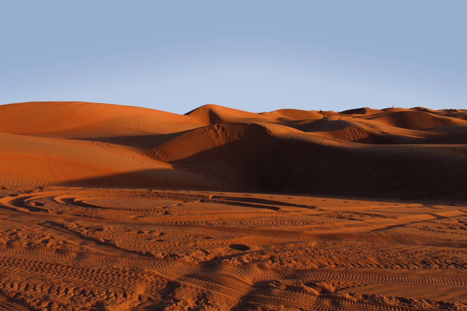 Orange sand dunes with tyre tracks under a pale blue sky in Oman