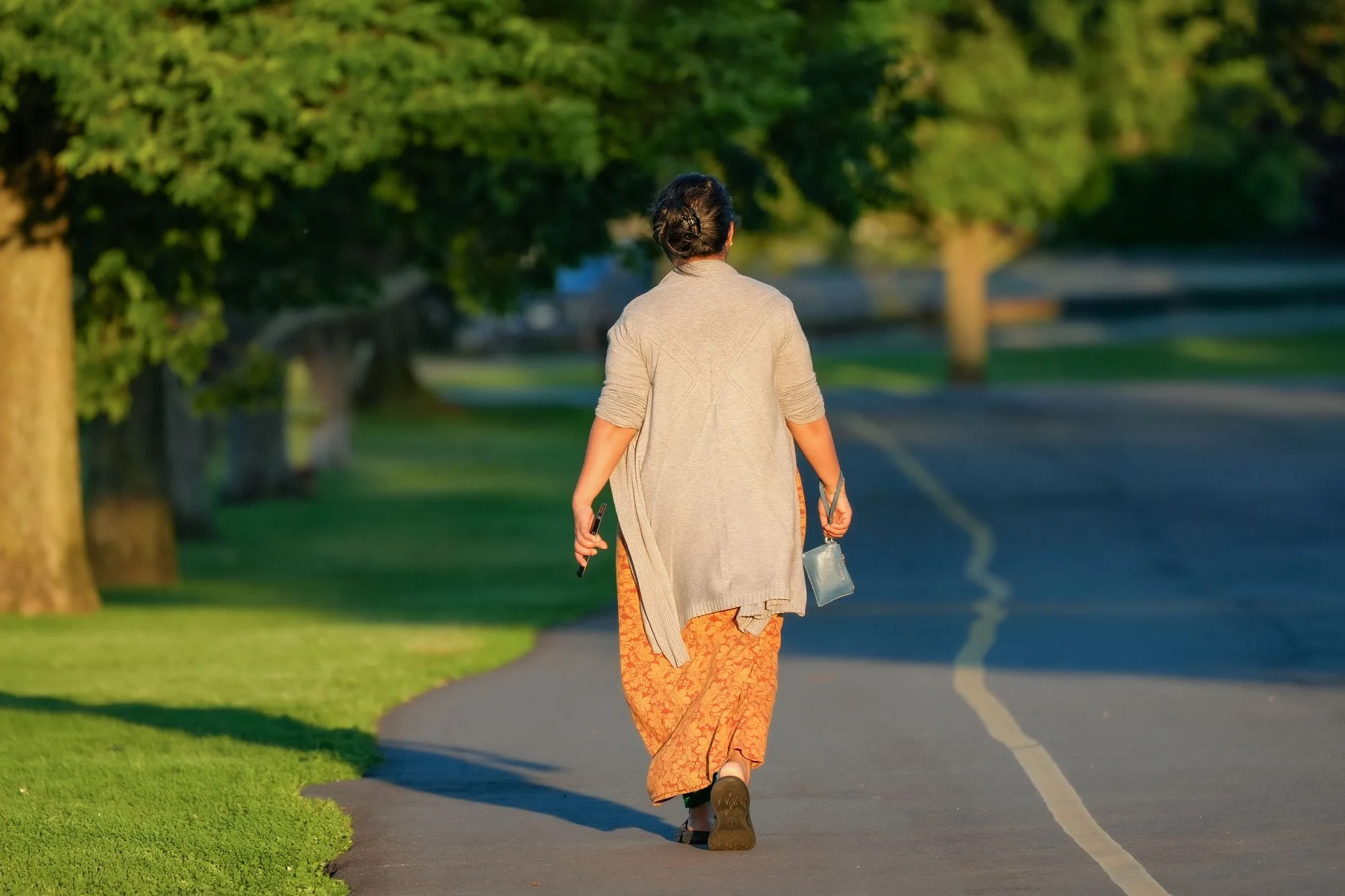 A woman walking along a tree-lined path in a park on a sunny morning