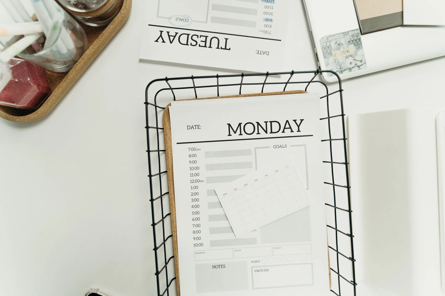 Printed daily planner sheets for Monday and Tuesday in a wire basket on a desk