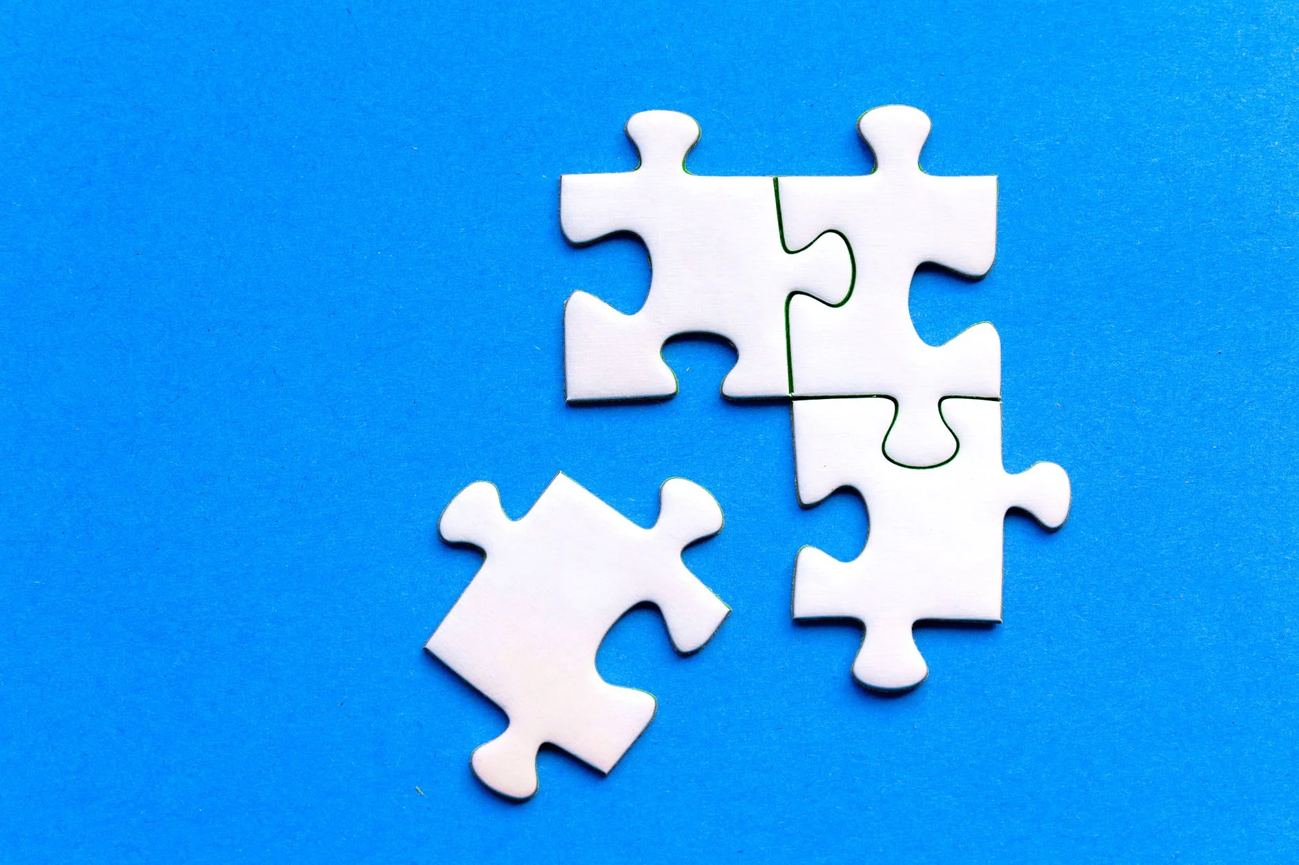 White jigsaw puzzle pieces, one separate from the rest, on a bright blue background