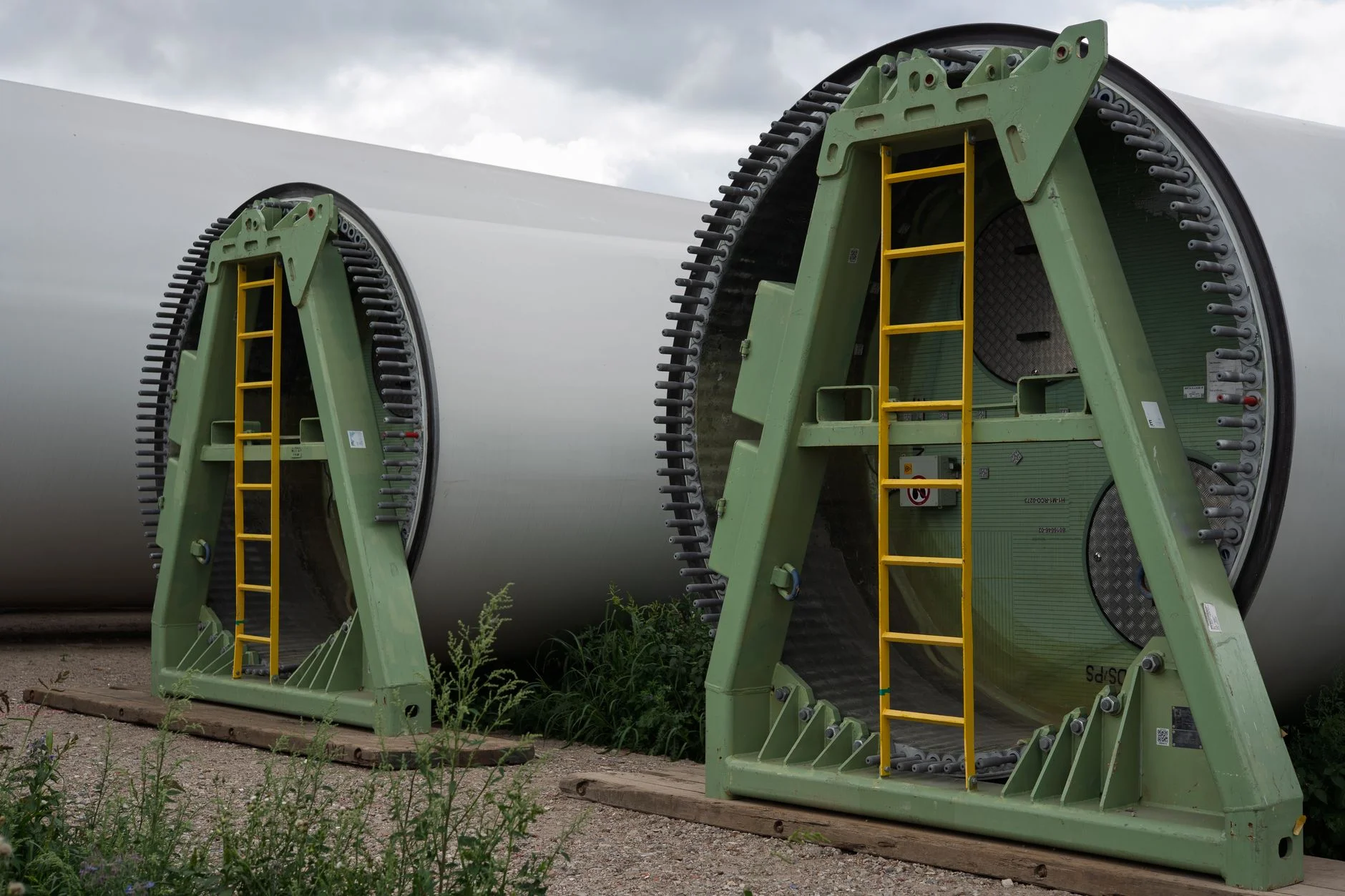 The round root ends of two huge wind turbine blades held in green metal transport frames