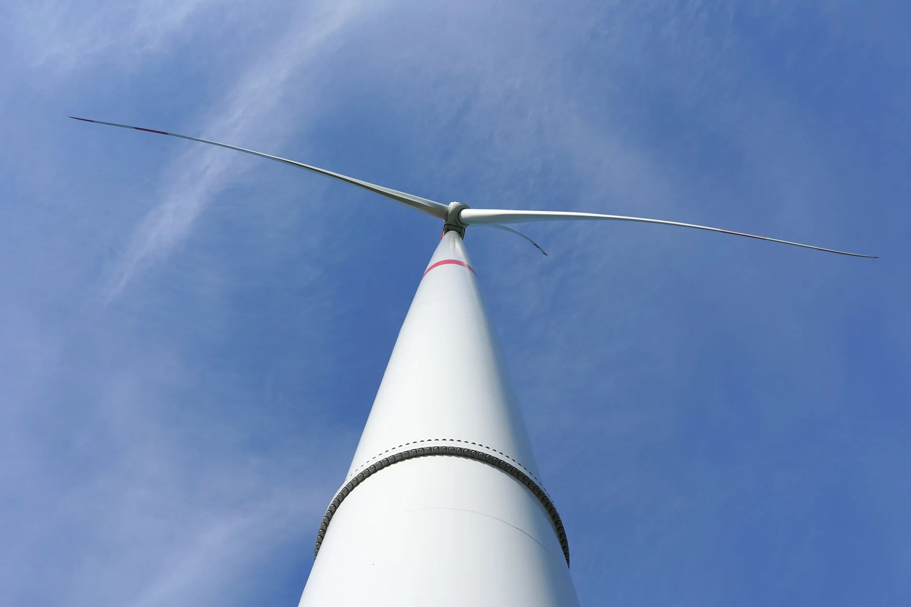 Looking straight up a white wind turbine tower to the nacelle and three long blades against a blue sky