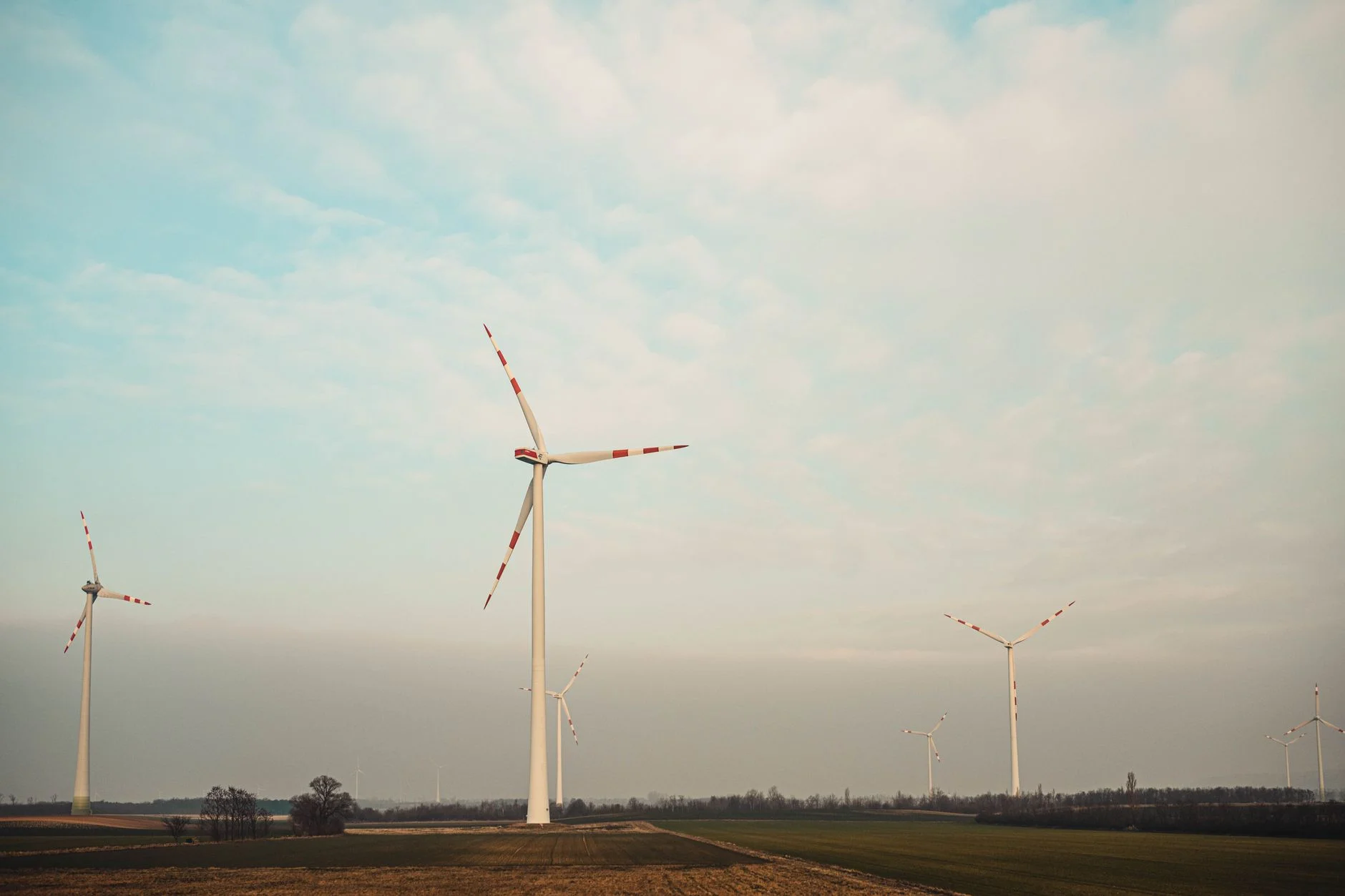 Three white wind turbines with red-tipped blades in a flat green field