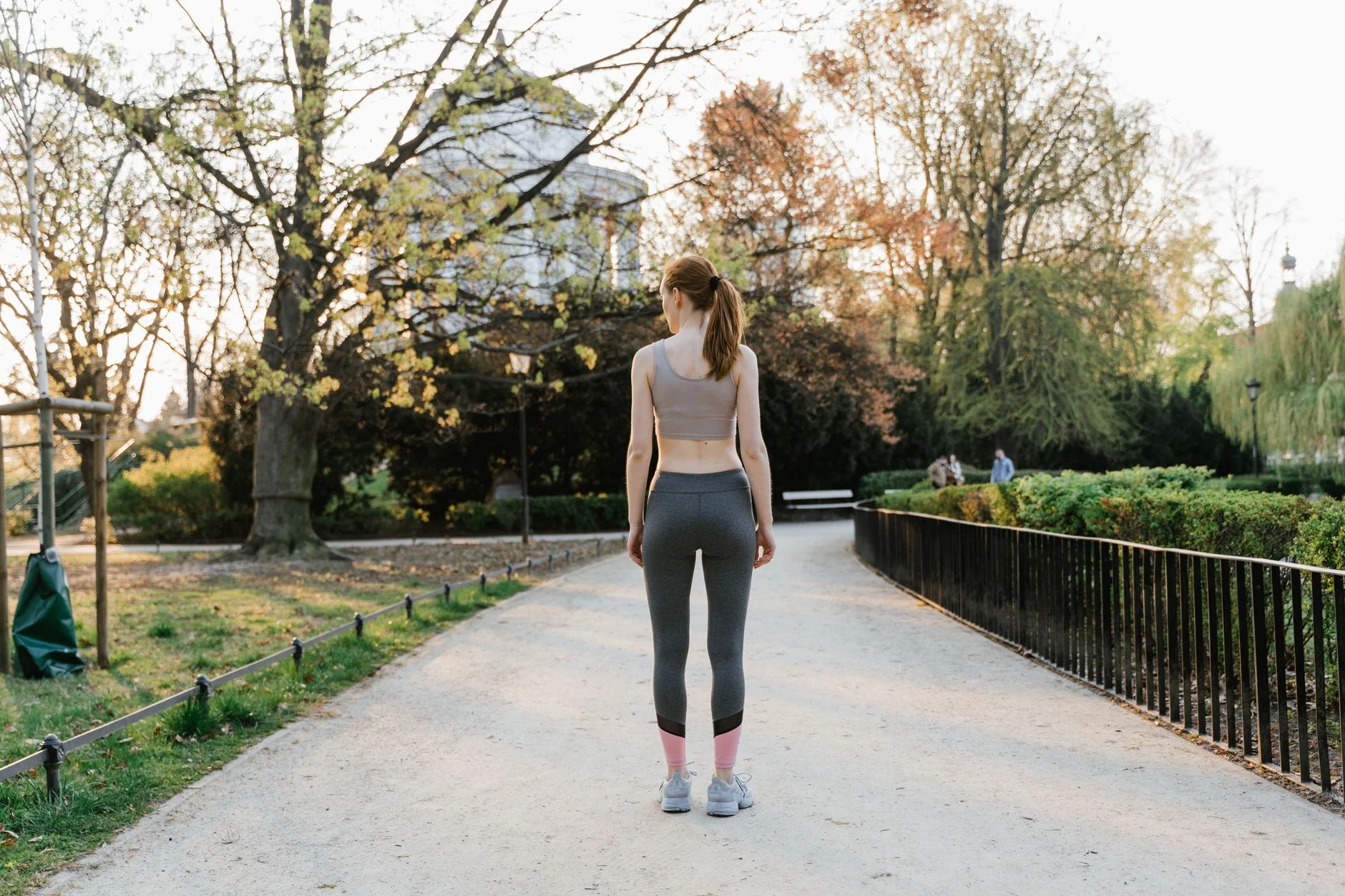 A woman in sports clothes standing on a gravel path in a park
