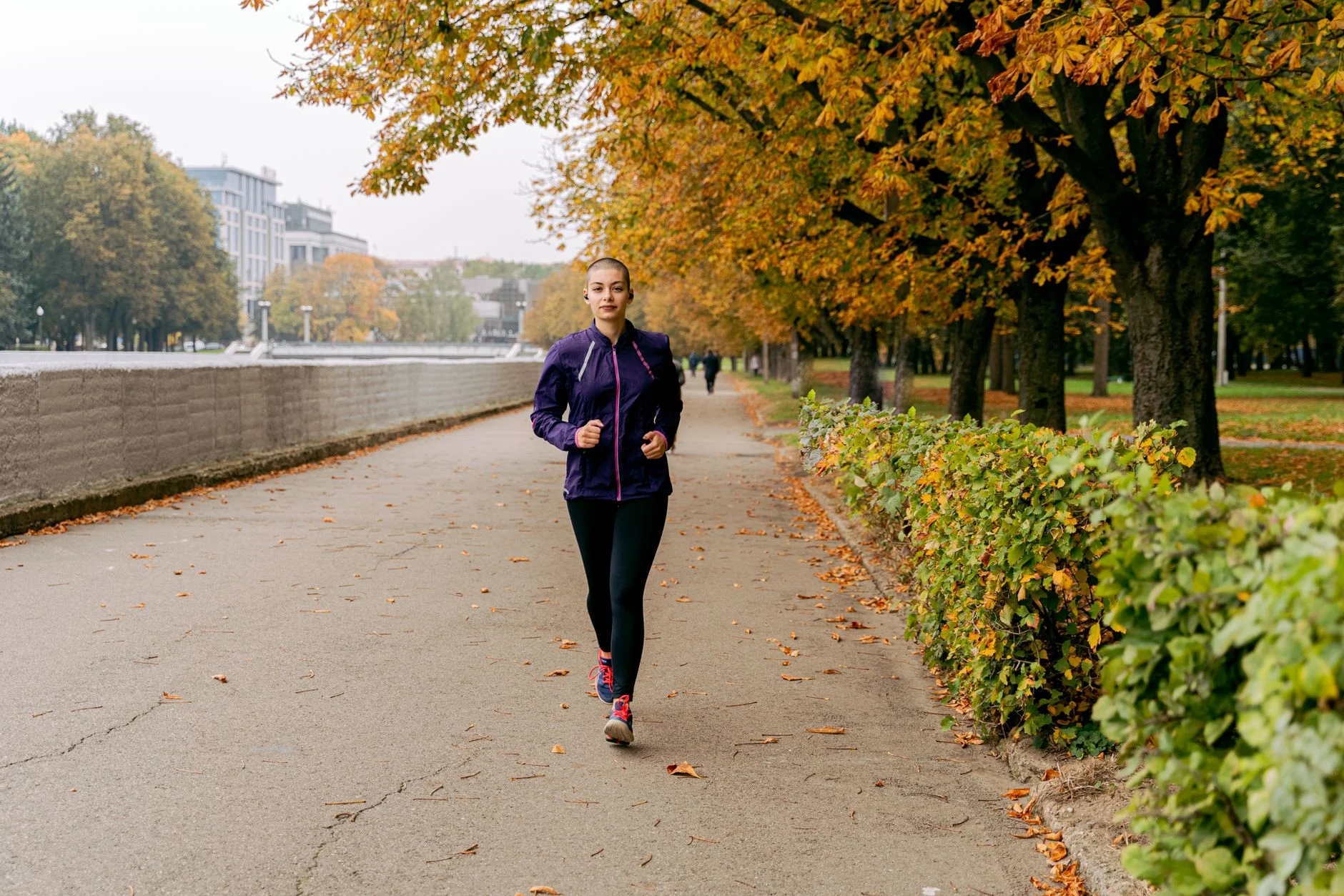 A woman jogging along a tree-lined path in a park in autumn