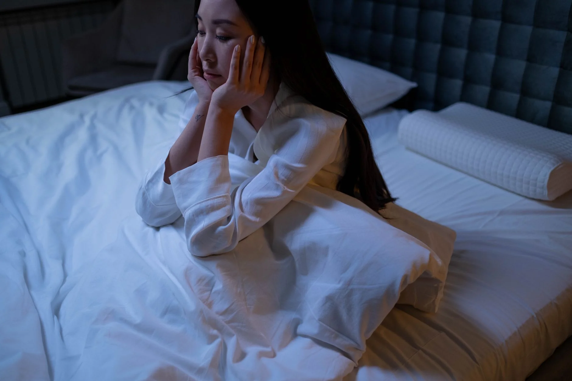 A young woman sitting awake in bed at night in a dim bedroom
