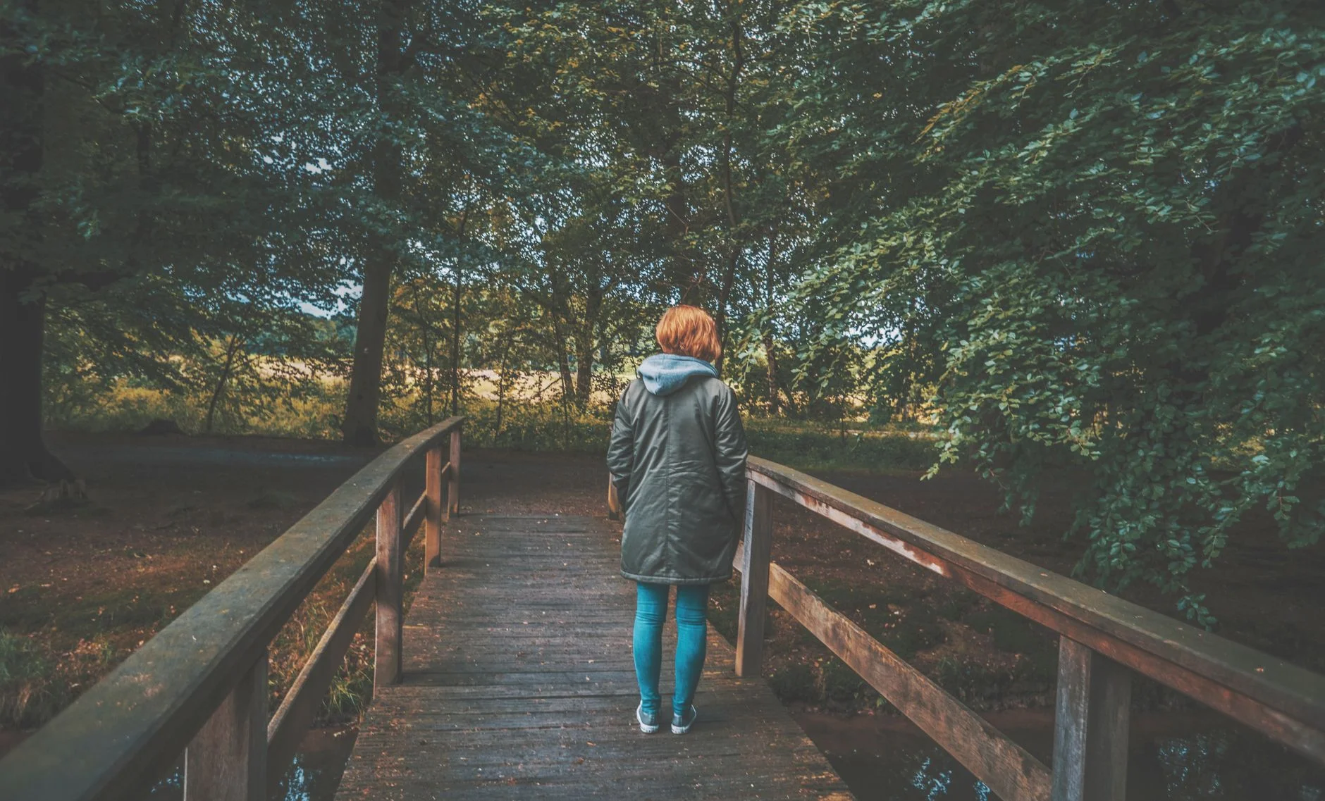 Woman standing alone on a wooden footbridge in a green wood