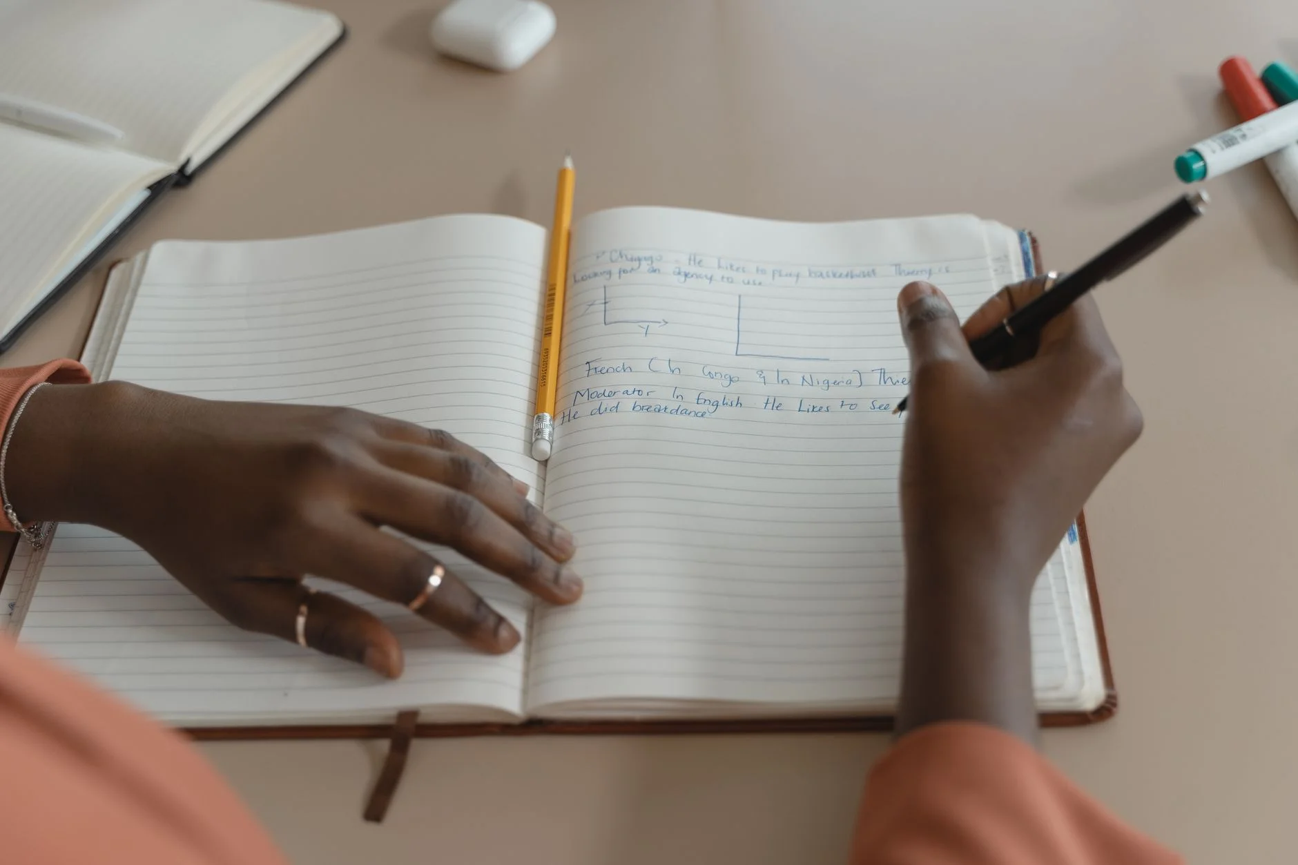 Hands writing in an open lined notebook on a desk